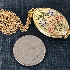 May include: Gold oval locket necklace with a floral design featuring red, yellow, and blue flowers and birds. The locket is open and the chain is visible. A US quarter is included for size reference.