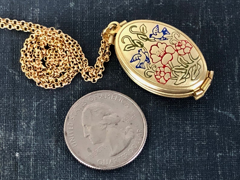 May include: Gold oval locket necklace with a floral design featuring red, yellow, and blue flowers and birds. The locket is open and the chain is visible. A US quarter is included for size reference.
