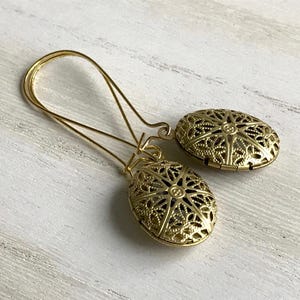 May include: A pair of gold filigree earrings with a delicate oval design. The earrings are made of metal and have a vintage look.
