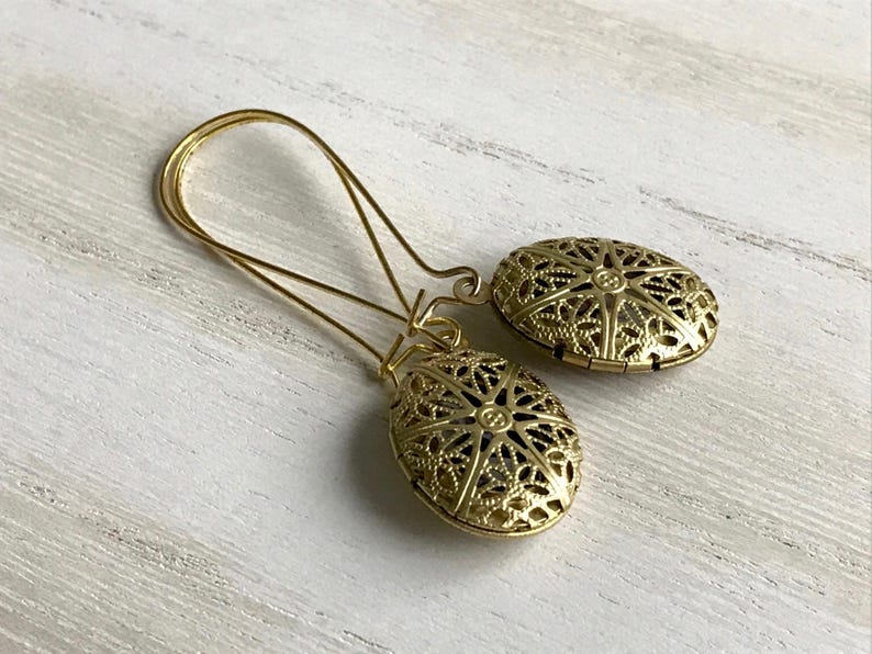 May include: A pair of gold filigree earrings with a delicate oval design. The earrings are made of metal and have a vintage look.