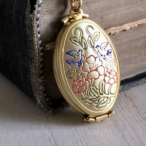 May include: Gold oval locket with a hinged closure. The locket features an enamel design of two blue birds and red flowers on a green stem.