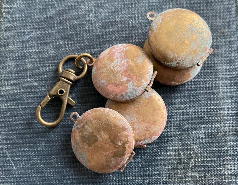 May include: A set of five small, round, brass-colored locket charms with a worn, distressed finish. The charms are attached to a brass-colored key ring.