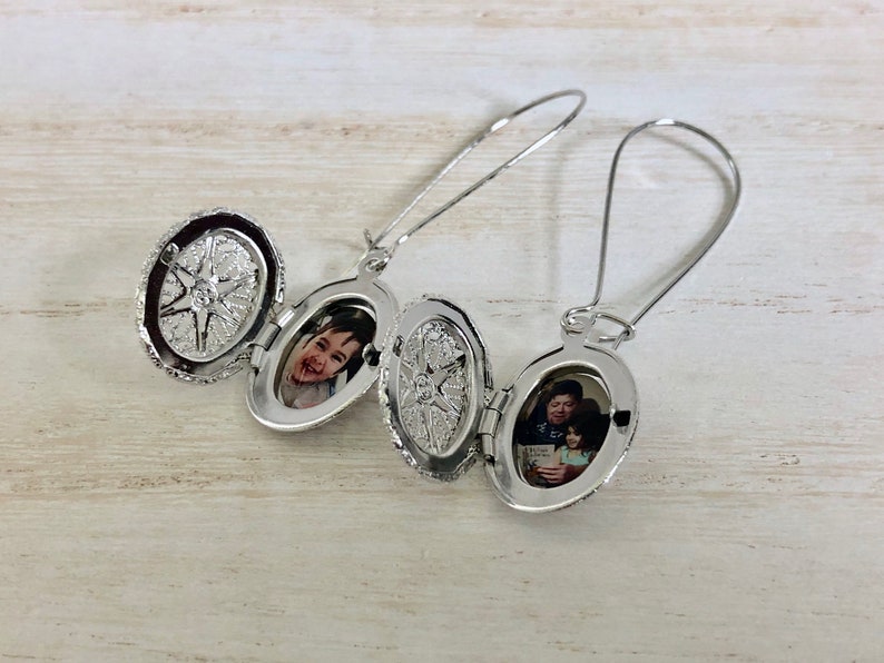 May include: A pair of silver locket earrings with a photo of a child and a photo of a man and child inside. The lockets are open and the photos are visible.
