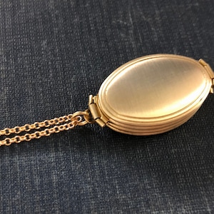 May include: A gold oval locket with a chain. The locket has a smooth, shiny surface and a hinged opening.