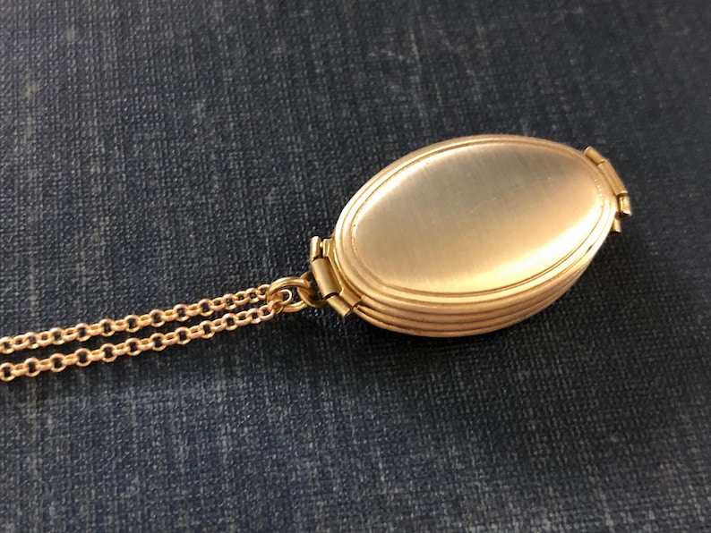 May include: A gold oval locket with a chain. The locket has a smooth, shiny surface and a hinged opening.