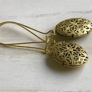 May include: A pair of gold filigree earrings with a delicate, intricate design. The earrings are dangle style and have a circular shape.