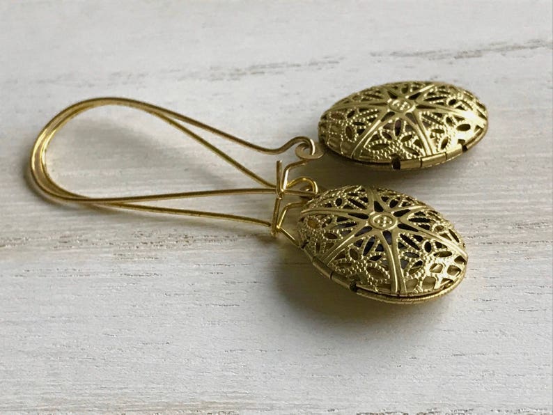 May include: A pair of gold filigree earrings with a delicate, intricate design. The earrings are dangle style and have a circular shape.