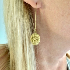 May include: Gold filigree earrings with a round, openwork design. The earrings are long and dangle from the earlobe.