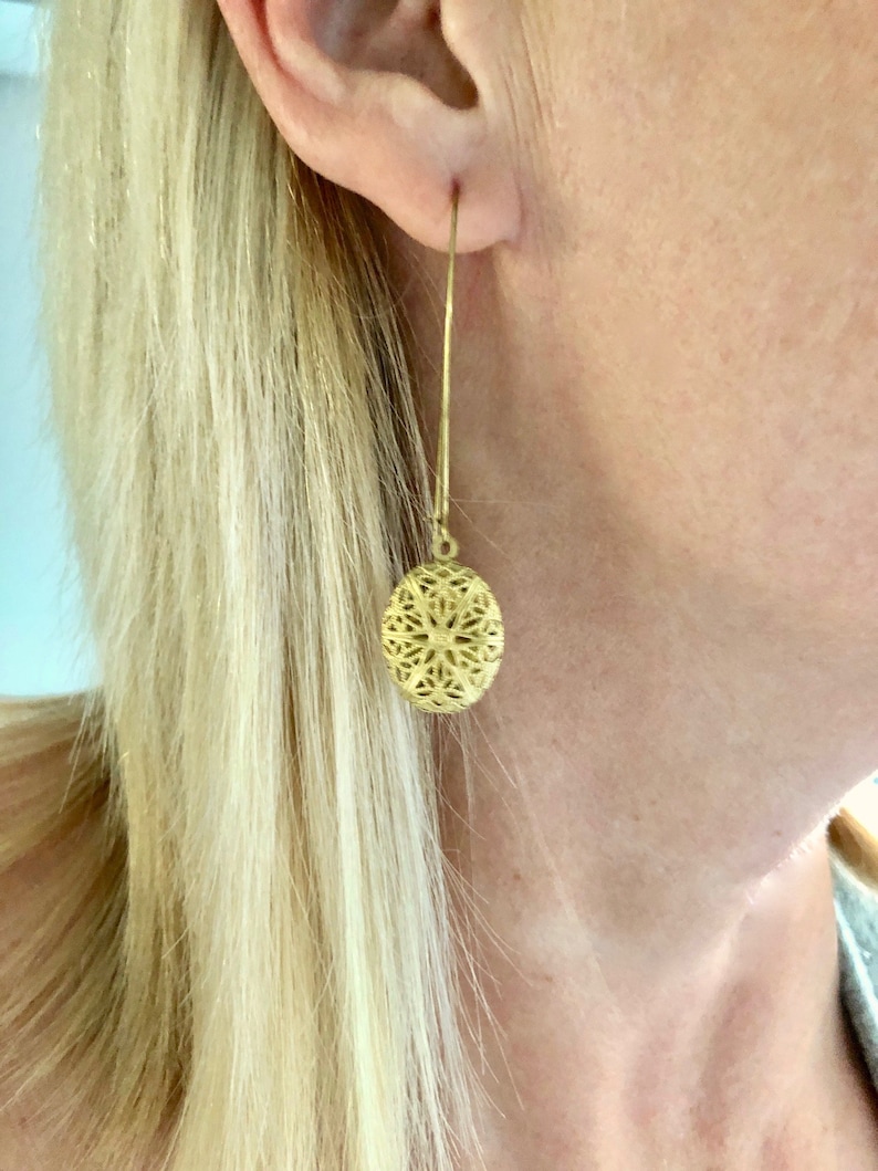May include: Gold filigree earrings with a round, openwork design. The earrings are long and dangle from the earlobe.