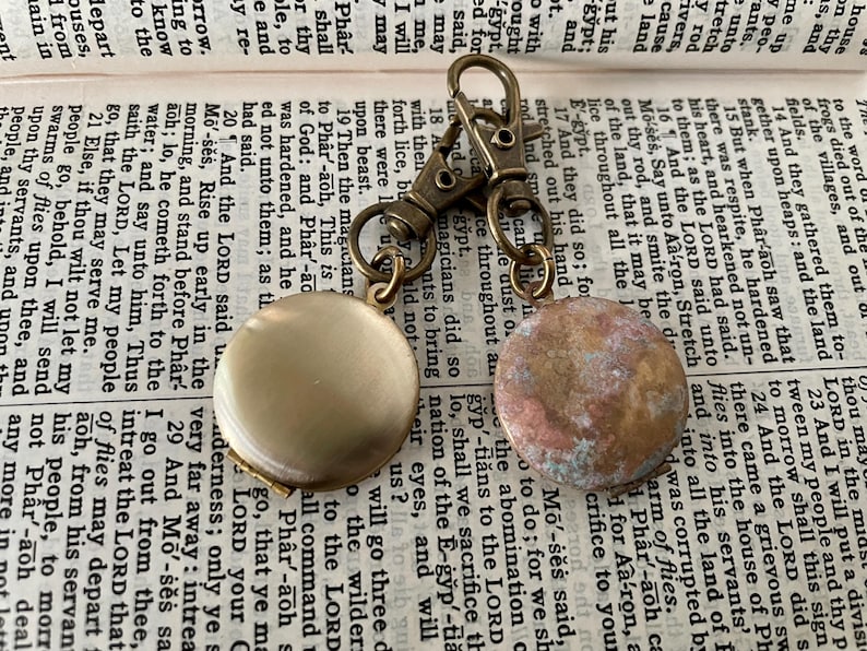 May include: A gold-toned keychain with two round, decorative charms. One charm is a smooth, light gold color, while the other is a textured, brown and white color.