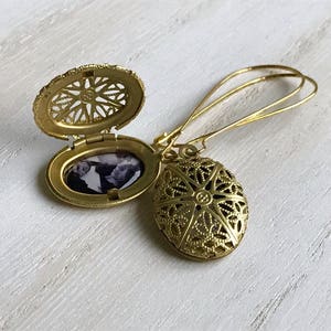 May include: Gold locket earrings with a filigree design. The locket opens to reveal a space for a photo.