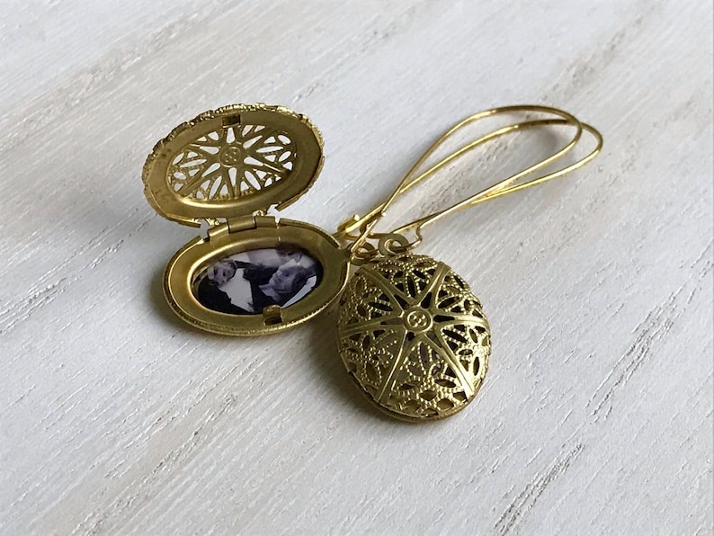 May include: Gold locket earrings with a filigree design. The locket opens to reveal a space for a photo.