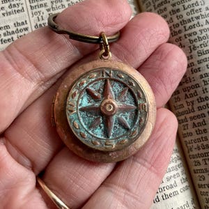 May include: A copper compass keychain with a blue and green patina. The compass has a raised star design and the letters N, S, E, and W are visible around the edge.