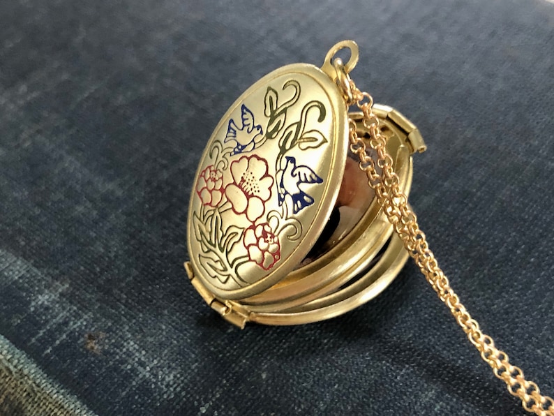 May include: A gold oval locket necklace with a floral design featuring red, pink, and blue flowers and birds. The locket is open, revealing a mirror inside.