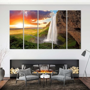 May include: A multi-panel canvas print featuring a scenic landscape with a waterfall cascading down a rocky cliff. The sky is a vibrant orange and pink sunset, with green hills and lush vegetation in the foreground.