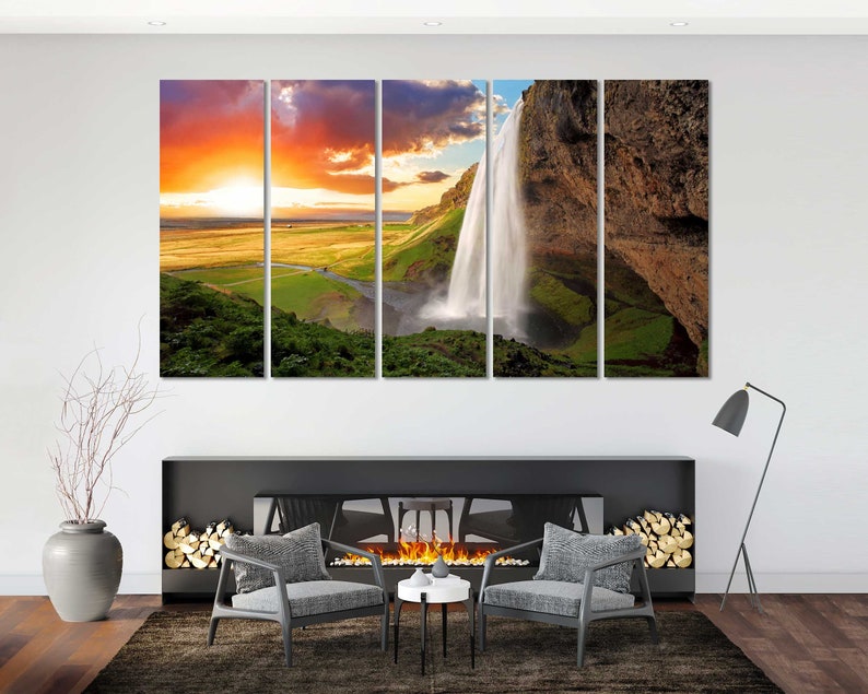 May include: A multi-panel canvas print featuring a scenic landscape with a waterfall cascading down a rocky cliff. The sky is a vibrant orange and pink sunset, with green hills and lush vegetation in the foreground.