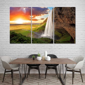 May include: A three-panel canvas print featuring a waterfall cascading down a rocky cliff. The waterfall is surrounded by lush green vegetation and a bright orange sunset in the background.