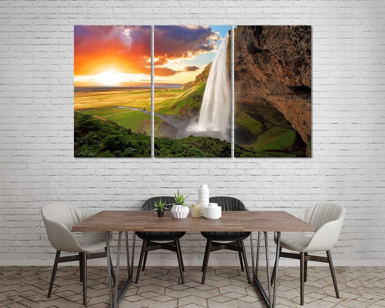 May include: A three-panel canvas print featuring a waterfall cascading down a rocky cliff. The waterfall is surrounded by lush green vegetation and a bright orange sunset in the background.