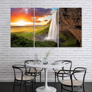 May include: A panoramic photograph of a waterfall cascading down a rocky cliff face. The waterfall is surrounded by lush green vegetation and a bright blue sky. The sun is setting in the distance, casting a warm glow over the scene.