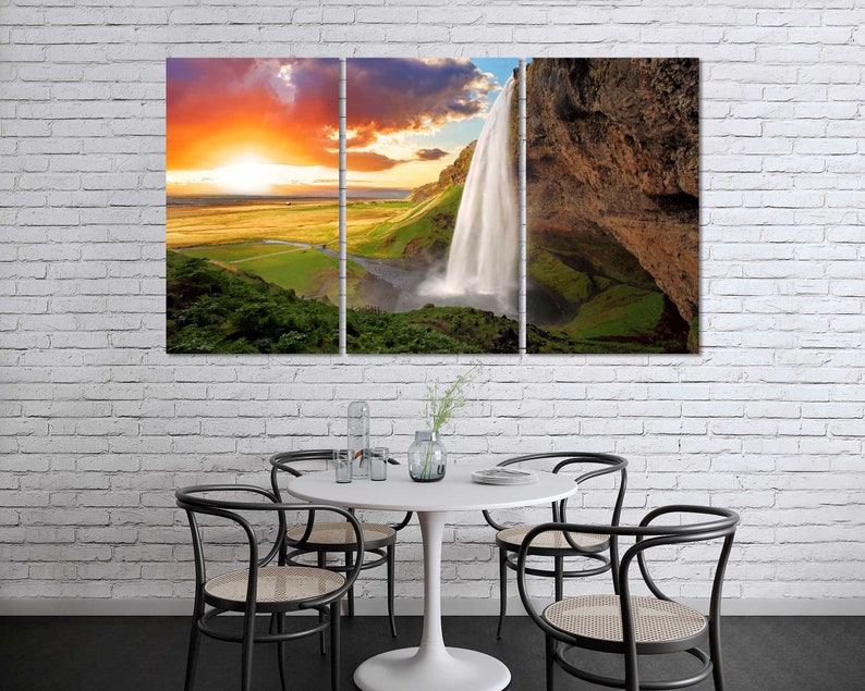 May include: A panoramic photograph of a waterfall cascading down a rocky cliff face. The waterfall is surrounded by lush green vegetation and a bright blue sky. The sun is setting in the distance, casting a warm glow over the scene.