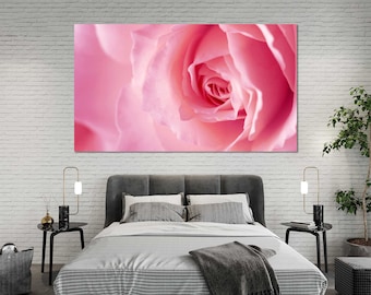 May include: A large canvas print featuring a close-up of a pink rose. The rose petals are soft and delicate, with a gradient of pink hues. The artwork is displayed above a bed with gray bedding and a white brick wall.