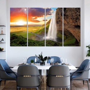 May include: A multi-panel canvas print featuring a scenic landscape with a waterfall cascading down a rocky cliff. The sky is a vibrant orange and yellow, with clouds in the background. The waterfall is surrounded by lush green vegetation.