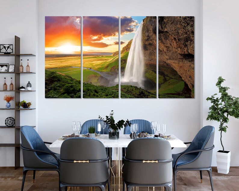 May include: A multi-panel canvas print featuring a scenic landscape with a waterfall cascading down a rocky cliff. The sky is a vibrant orange and yellow, with clouds in the background. The waterfall is surrounded by lush green vegetation.