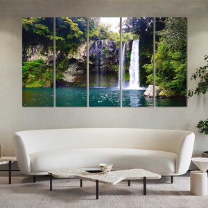 May include: A panoramic photograph of a waterfall cascading down a rocky cliff face, surrounded by lush green foliage. The water is clear and blue, and the surrounding vegetation is vibrant and healthy.