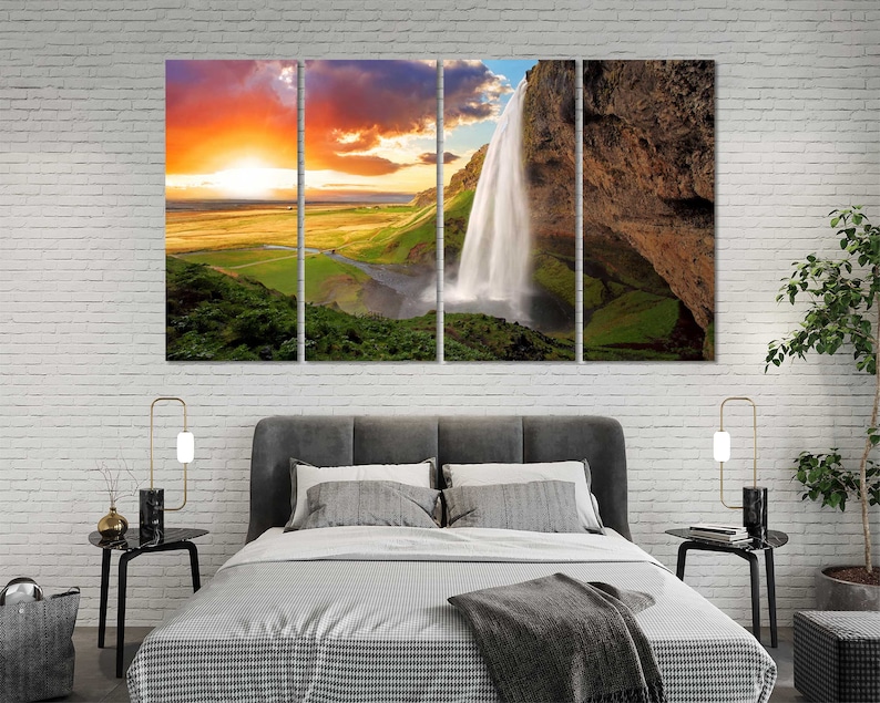 May include: A multi-panel canvas print featuring a scenic landscape with a waterfall cascading down a rocky cliff. The sky is a vibrant orange and yellow, with clouds in the background. The scene is framed by lush green vegetation.