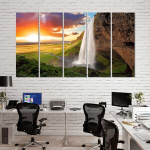 May include: A multi-panel canvas print featuring a scenic landscape with a waterfall cascading down a rocky cliff. The sky is a vibrant orange and pink, with clouds in the distance. The waterfall is surrounded by lush green vegetation.