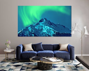 May include: A large canvas print showing a snow-covered mountain range beneath a vivid green aurora borealis. The artwork is displayed above a navy blue sofa with cushions, a round coffee table, and a patterned rug.