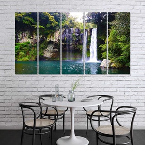 May include: A panoramic view of a waterfall cascading down a rocky cliff face, surrounded by lush green foliage. The water is clear and blue, and the surrounding vegetation is vibrant and verdant.