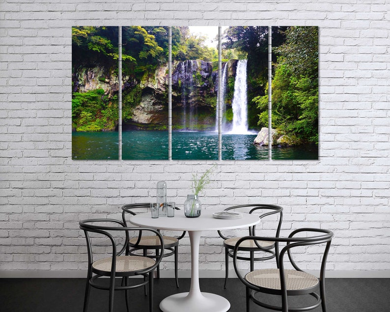 May include: A panoramic view of a waterfall cascading down a rocky cliff face, surrounded by lush green foliage. The water is clear and blue, and the surrounding vegetation is vibrant and verdant.