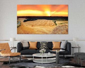 May include: A scenic landscape photograph of a field of hay bales at sunset. The sun is setting behind the bales, casting a warm glow over the scene. The bales are scattered across the field, with some in the foreground and others in the distance.