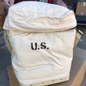 May include: A large, white canvas bag with a zippered top and a black strap. The bag has a black "U.S." printed on the front.