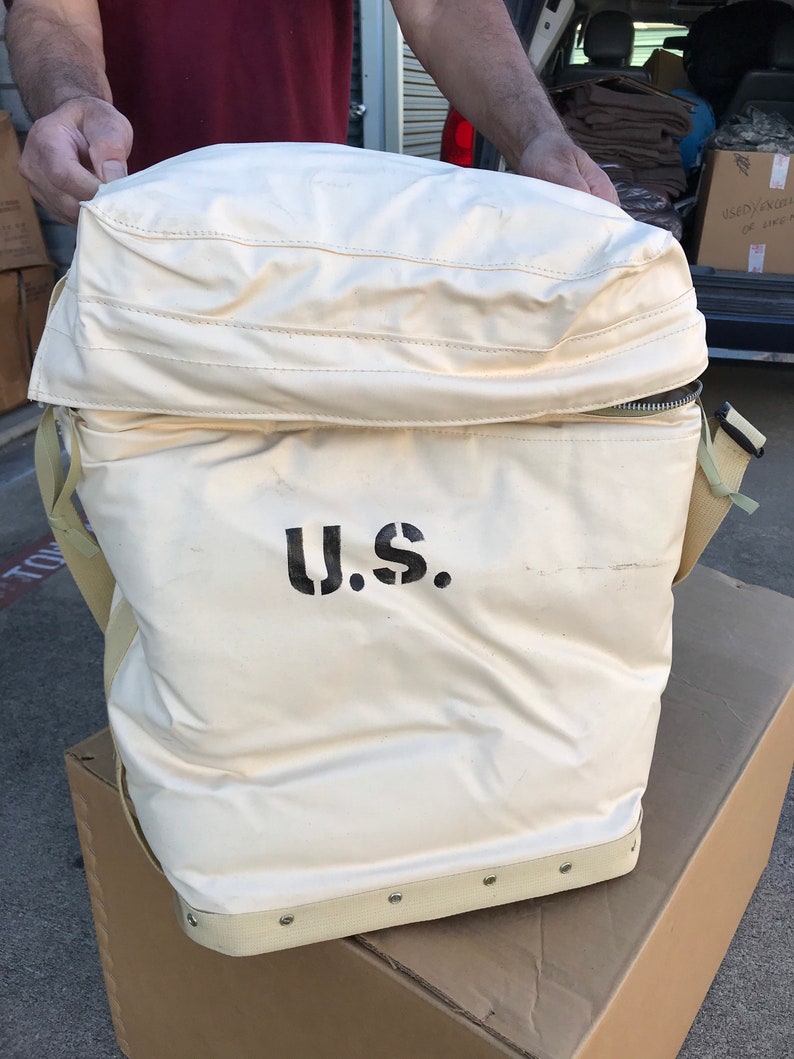 May include: A large, white canvas bag with a zippered top and a black strap. The bag has a black "U.S." printed on the front.