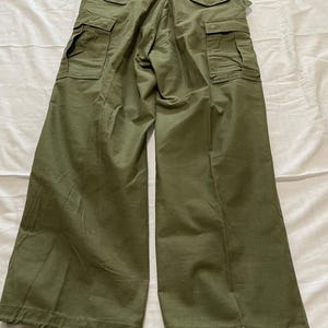 May include: Olive green cargo pants with multiple pockets and adjustable waist tabs. The pants have a relaxed fit and drawstring closures at the ankles. The image shows the back of the pants.