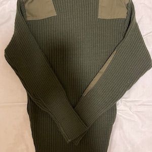 Może przedstawiać: Zielony, prążkowany sweter z dzianiny z dwoma oliwkowymi naszywkami na ramionach.