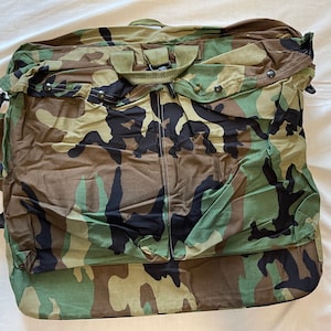 May include: A camouflage-patterned duffel bag with a black shoulder strap and a zipper closure.