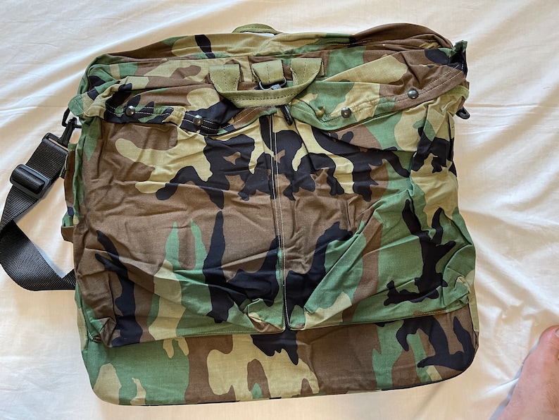 May include: A camouflage-patterned duffel bag with a black shoulder strap and a zipper closure.