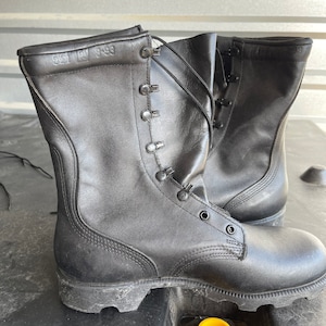 Puede incluir: Un par de botas de cuero negro con cordones y suela de goma gruesa. Las botas tienen una etiqueta "Talla 9-88" en el lateral.