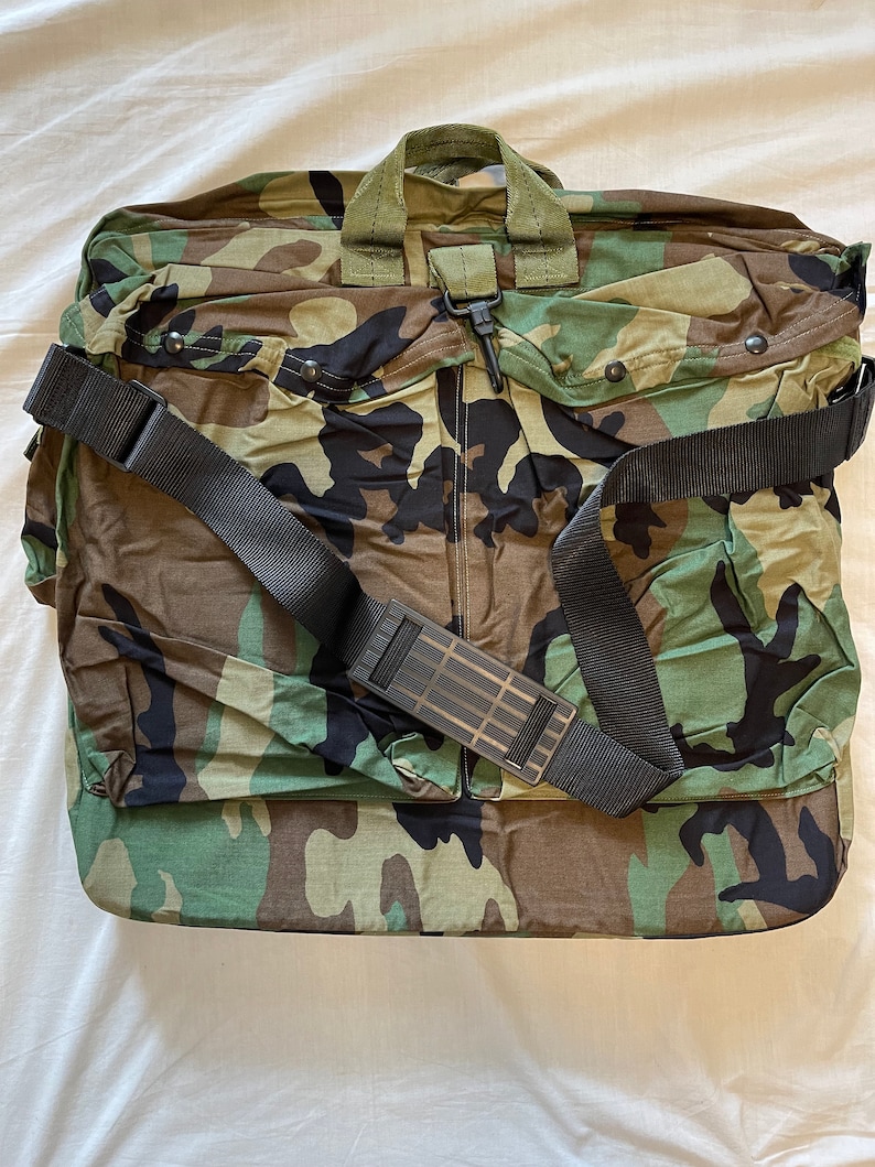 May include: A camouflage green duffel bag with a black shoulder strap and a zip closure.