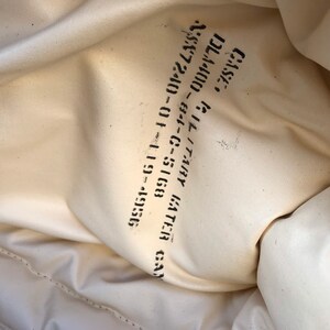 May include: Close-up of a white fabric bag with black text that reads "GATHER GA 95357-5168 01-11-5168 C-5168Y 82-81-C-7344Y GATHER GA 2/SK 72400 - 01 11 5168 DL44000"