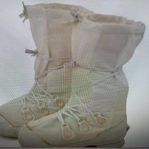 Puede incluir: Un par de botas blancas de lona con cordones y hebillas. Las botas son altas y tienen una punta redonda.
