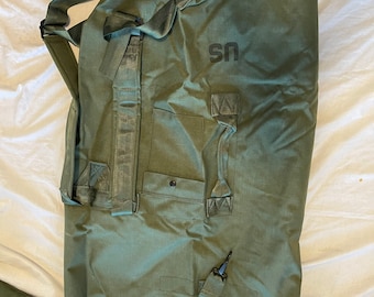 May include: A green canvas duffel bag with a black strap and a black "US" logo. The bag has a zippered pocket and a handle.