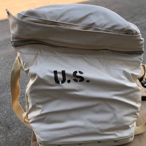 May include: A white canvas bag with a zipper closure and a black "U.S." stencil. The bag has a brown leather strap and a white canvas strap.