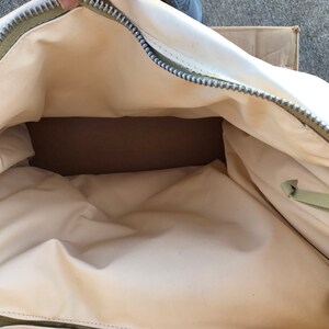 May include: A white canvas duffel bag with a green zipper and a green strap. The bag is open and empty.