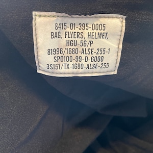 May include: A green label with white text containing the following information: 8415-01-395-0005 BAG, FLYERS, HELMET, HGU-56/P 81996/1680-ALSE-255-1 SP0100-99-D-6000 3S151/TX-1680-ALSE-255