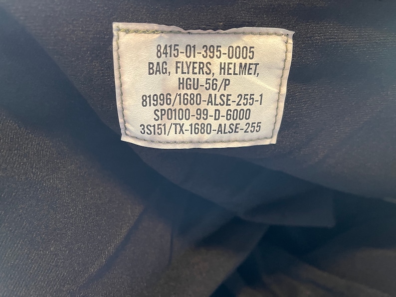 May include: A green label with white text containing the following information: 8415-01-395-0005 BAG, FLYERS, HELMET, HGU-56/P 81996/1680-ALSE-255-1 SP0100-99-D-6000 3S151/TX-1680-ALSE-255