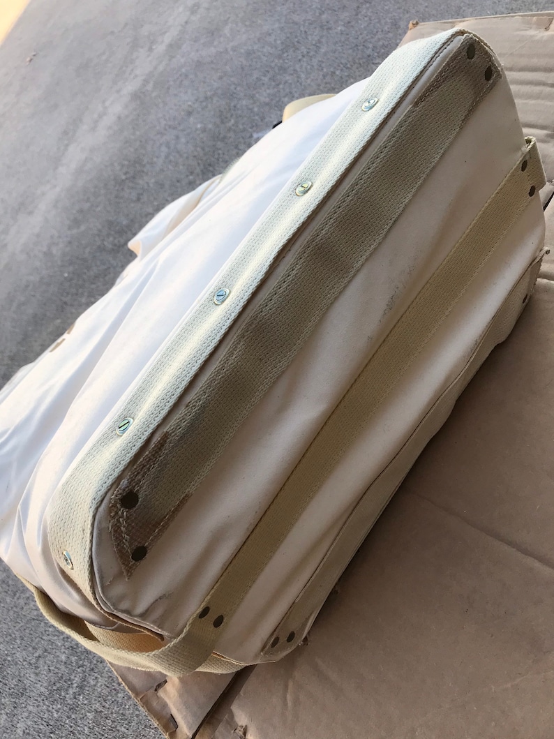 May include: A white canvas tote bag with reinforced seams and multiple straps. The bag has a cream colored canvas trim and is secured with metal rivets.